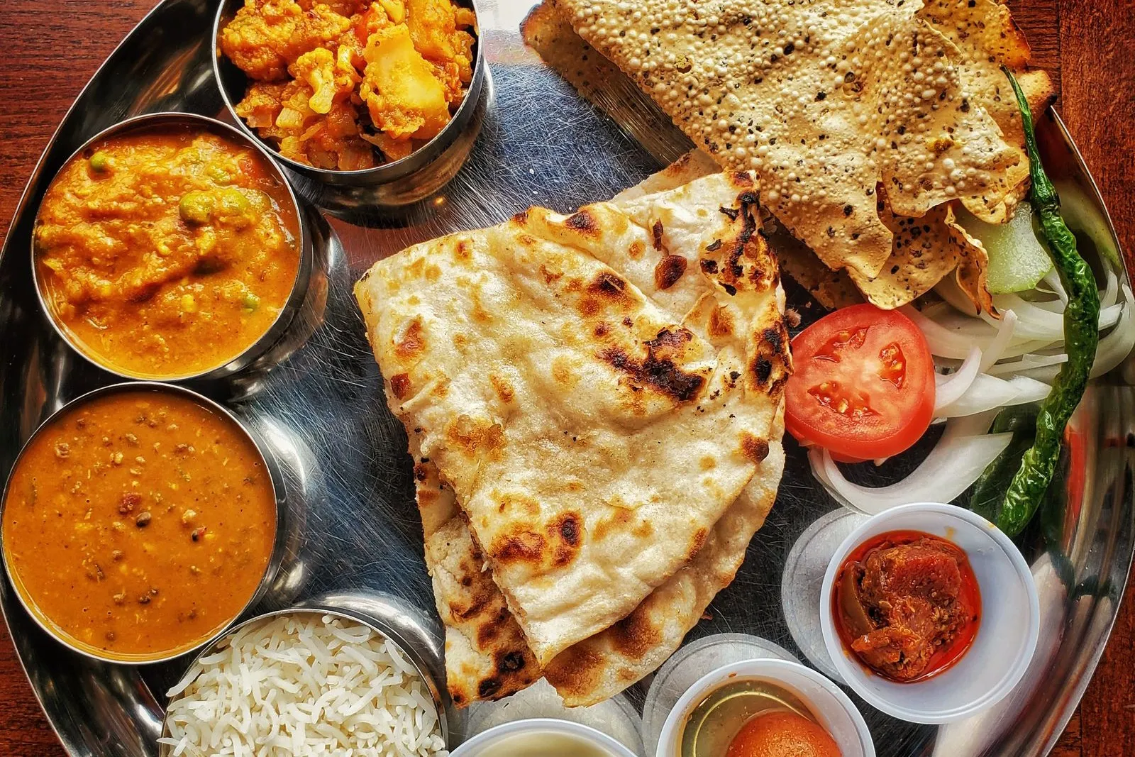 A thali with naan, dal, paneer curry, rice and papad